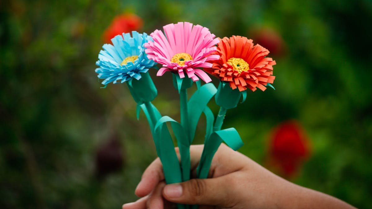 Main d'enfant tenant un bouquet de fleurs en papier coloré bleu rose et orange