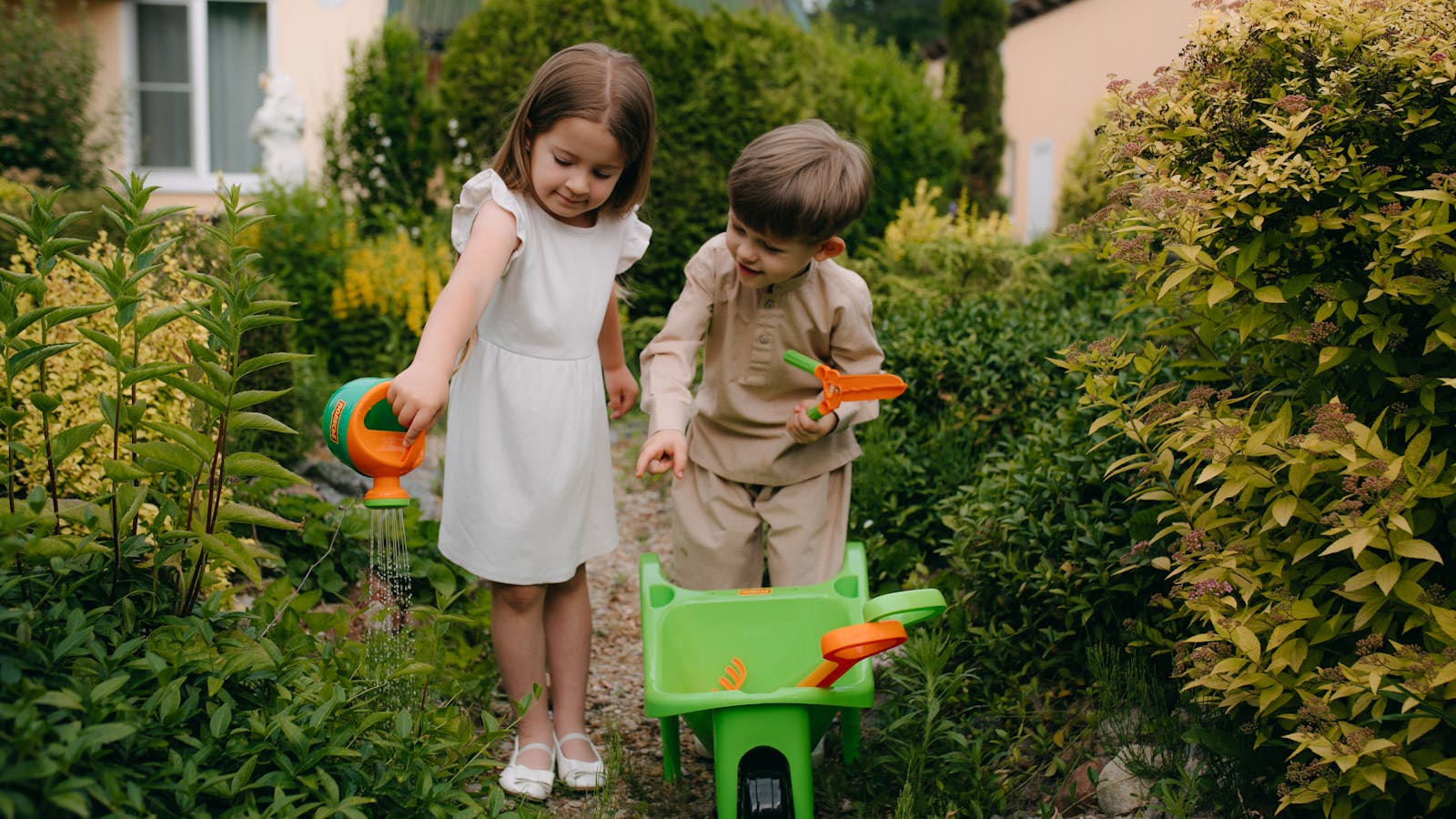Enfants arrosant le jardin avec un arrosoir jouet et une brouette en extérieur