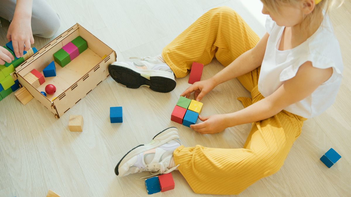 Choisir le bon jeu de construction selon l'âge Enfant en jaune jouant avec des blocs de construction colorés sur le sol